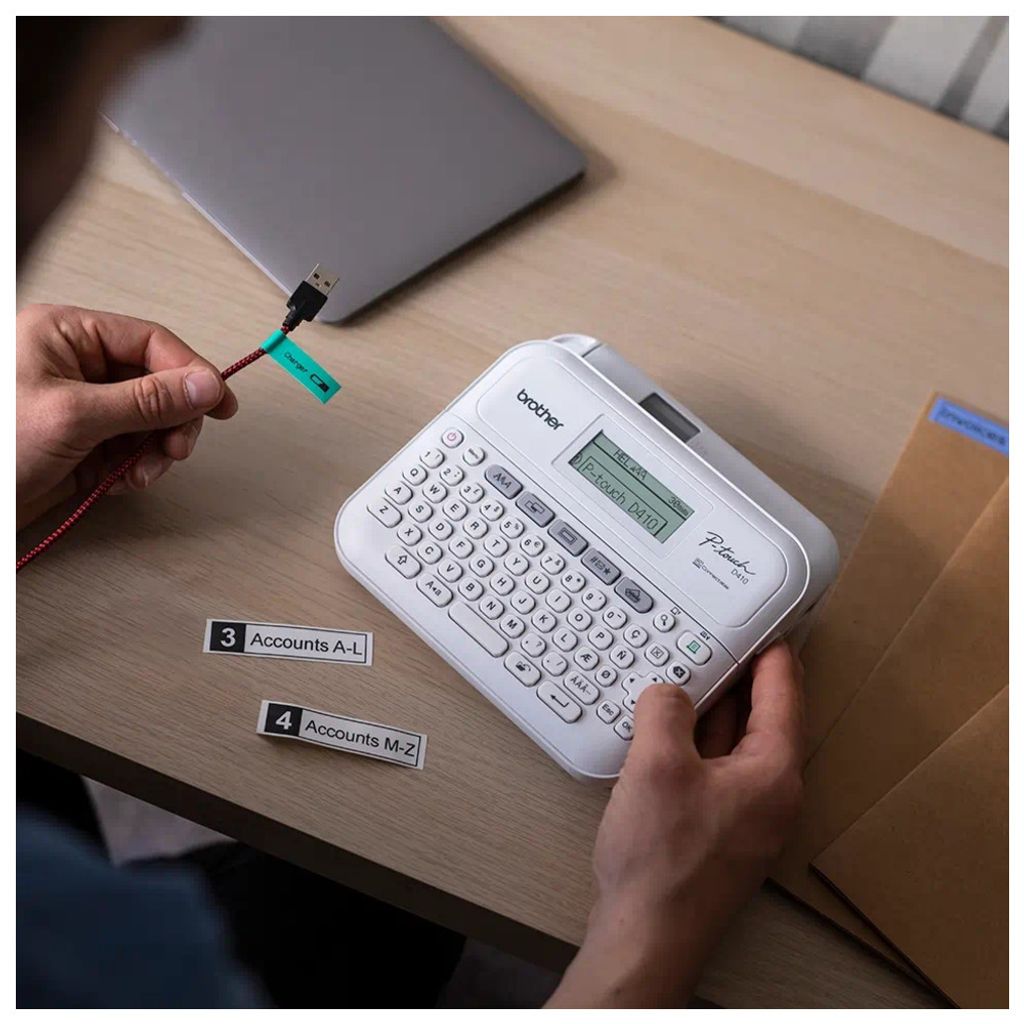 A person is using a Brother P-touch D410 label maker to label a red cable connected to a laptop.