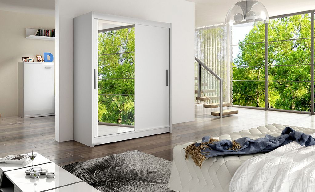 A modern bedroom with a white wardrobe with mirrored doors, a bed with white bedding, and a large window overlooking a lush green garden.