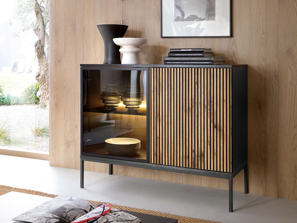 A modern sideboard with a glass door and a slatted wooden door, displayed in a well-lit room with wooden walls and a large window.
