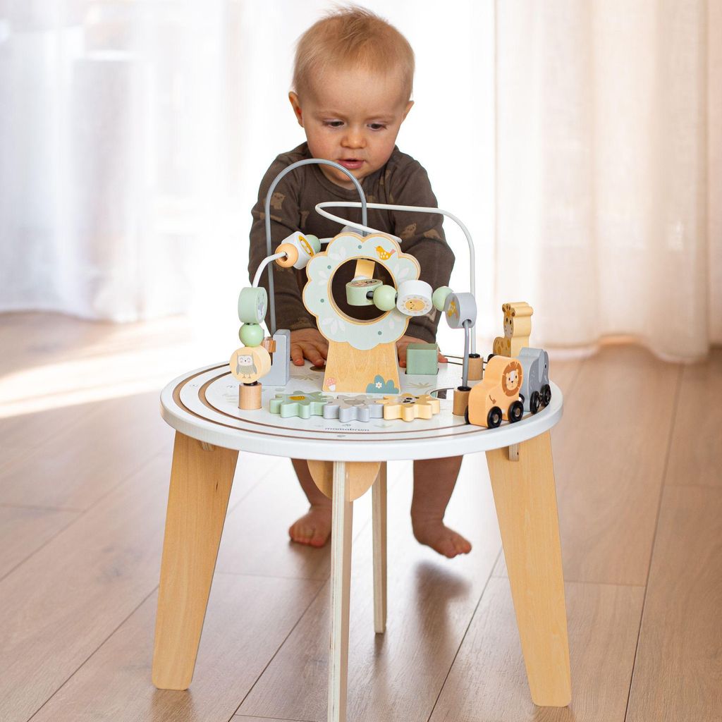 A baby is playing with a wooden activity table with a magnetic train and bead maze.
