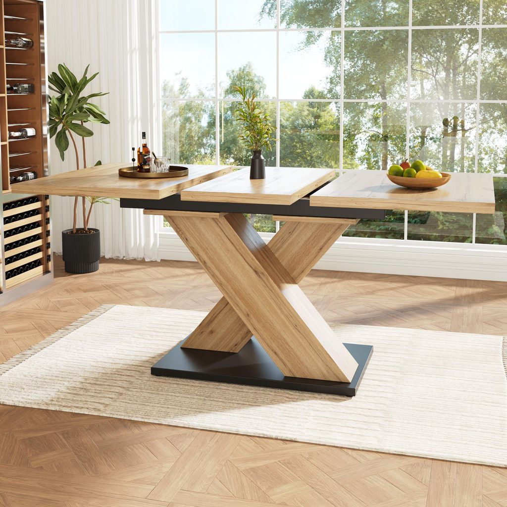 A dining room with a large wooden extendable table in the center, set against a backdrop of large windows overlooking greenery. A wine rack is visible on the left.