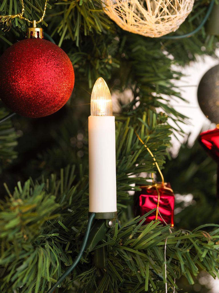 A close-up of a Christmas tree with decorations, including a lit candle-shaped LED light.