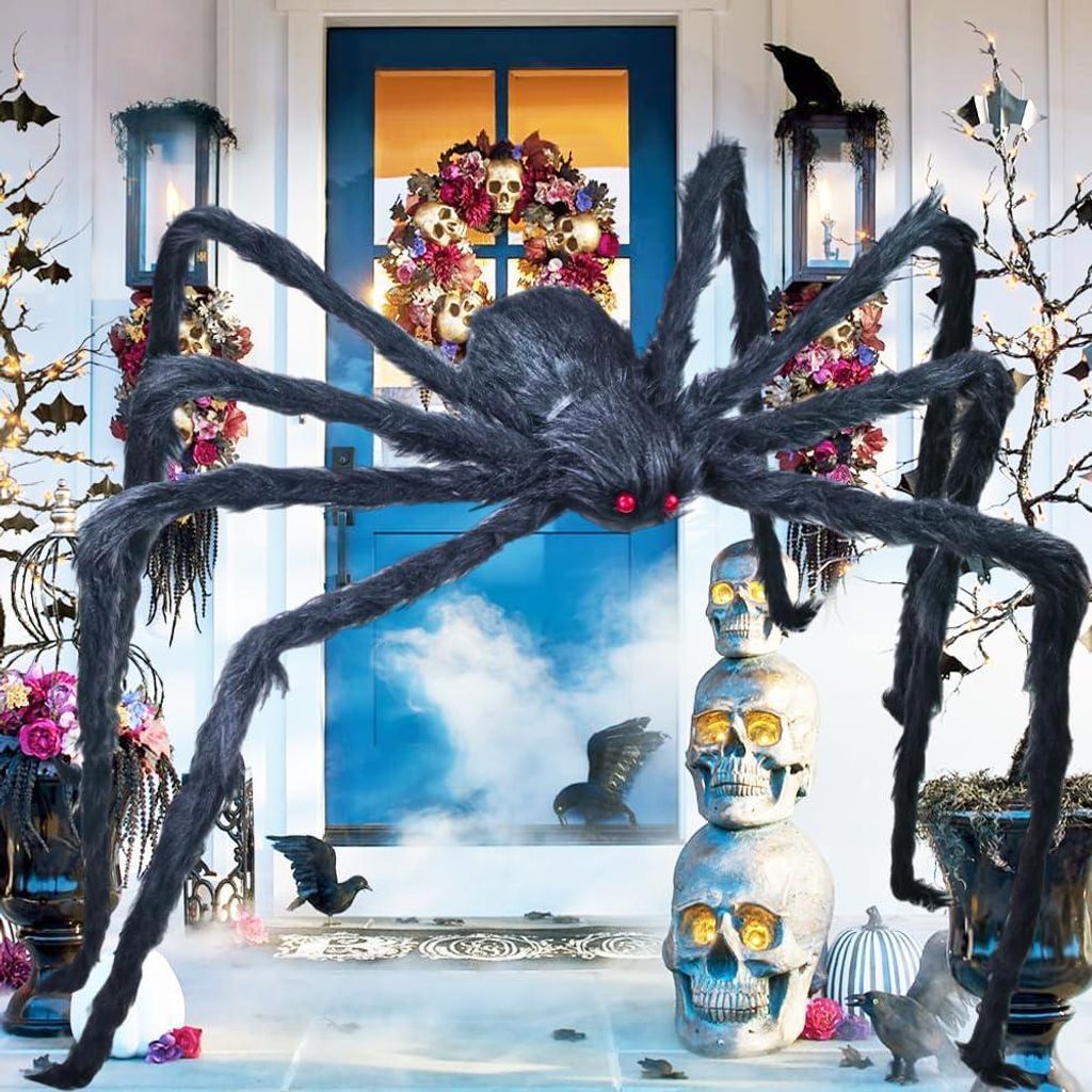 A Halloween decoration scene featuring a large, furry spider, stacked skulls, and floral arrangements in front of a blue door.