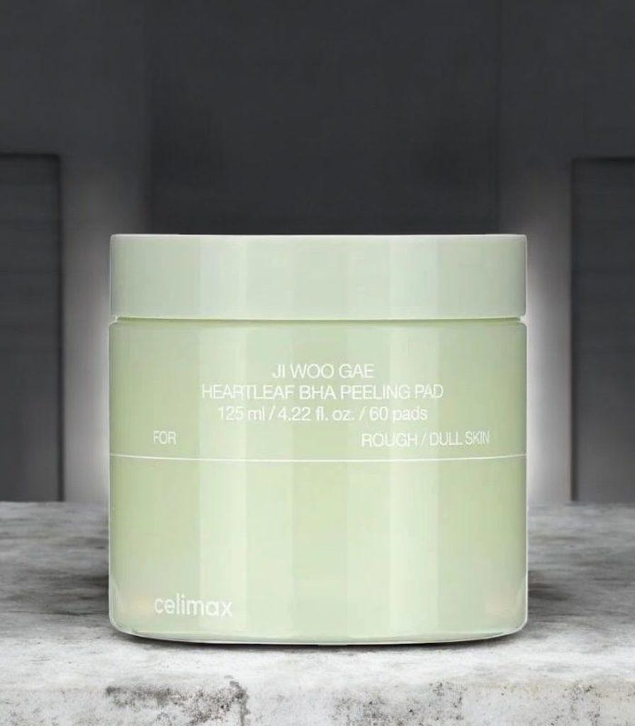 A light green jar of skincare pads sits on a textured surface with a blurred background.