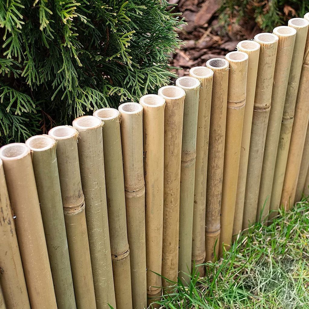 A close-up view of a bamboo border fence separating a garden bed from grass and mulch.
