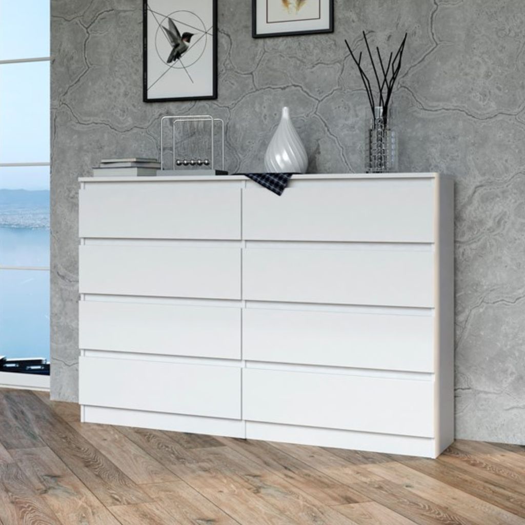 A white dresser with eight drawers is shown in a room with a gray textured wall and a wooden floor.