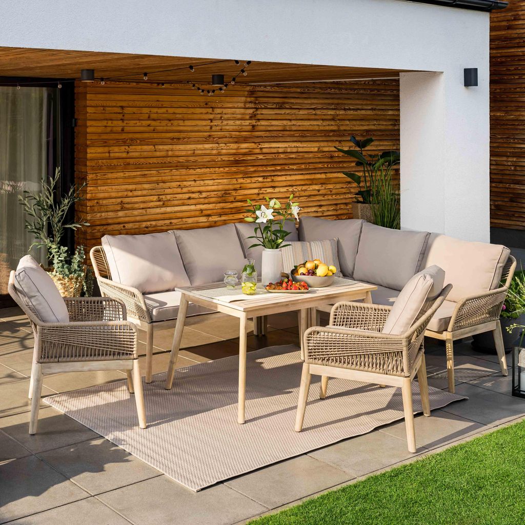 A patio furniture set is arranged on a tiled patio area, with a wooden wall in the background and grass in the foreground.