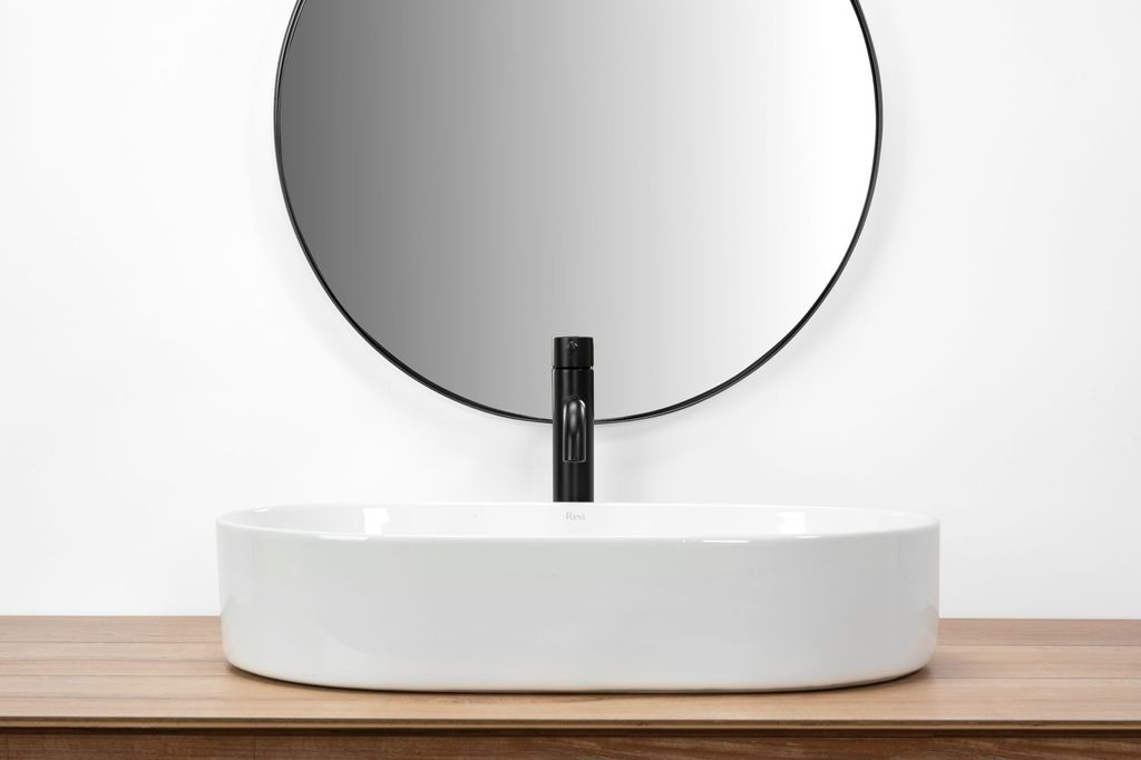 A white oval countertop sink with a black faucet is shown in a bathroom setting.