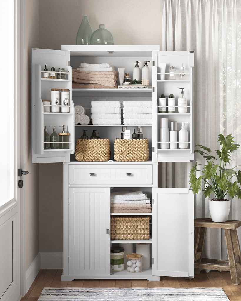 A white storage cabinet filled with various bathroom and home goods, with a potted plant to the right.