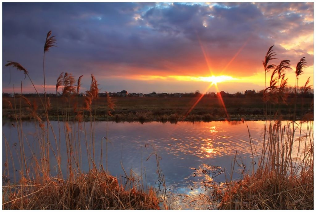 Wallario Premium Glasbild, freischwebende Optik, kräftige Farben, Größe 90 x 60 cm Motiv Sonnenuntergang über dem Fluss, Gräser im Wind