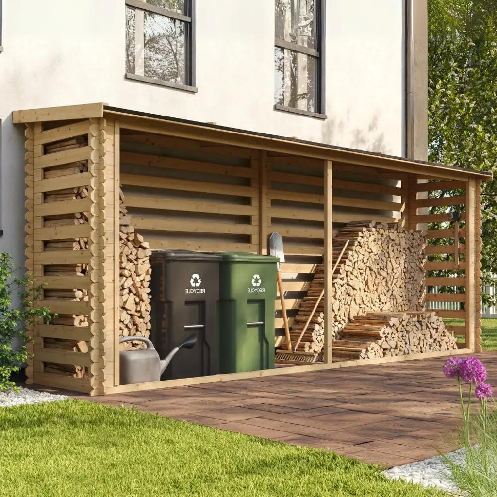A wooden log store filled with firewood, next to two recycling bins and a watering can, situated on a paved patio area next to a house.
