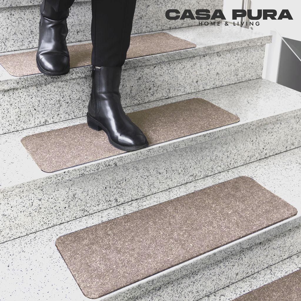 A person wearing black boots walks down a staircase with beige stair mats.