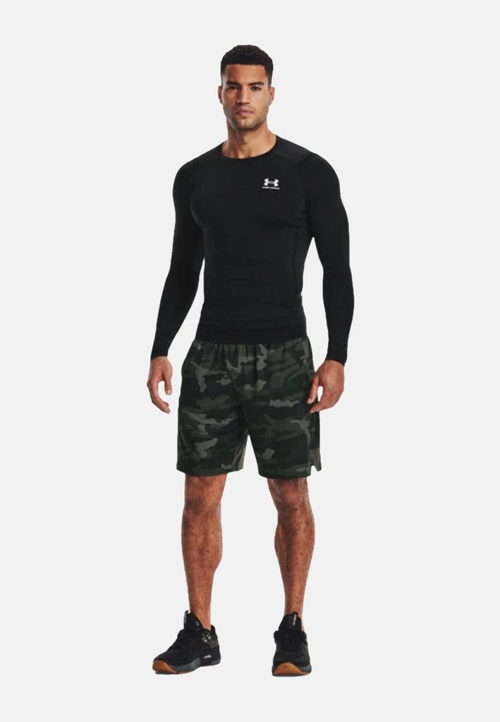 A man wearing a black long-sleeved shirt and camouflage shorts stands against a white background.