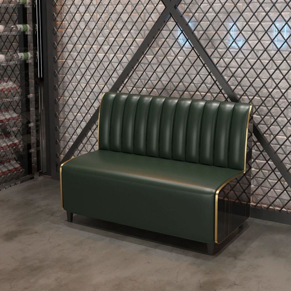 A green sofa with gold trim sits in front of a textured wall and a metal grate.