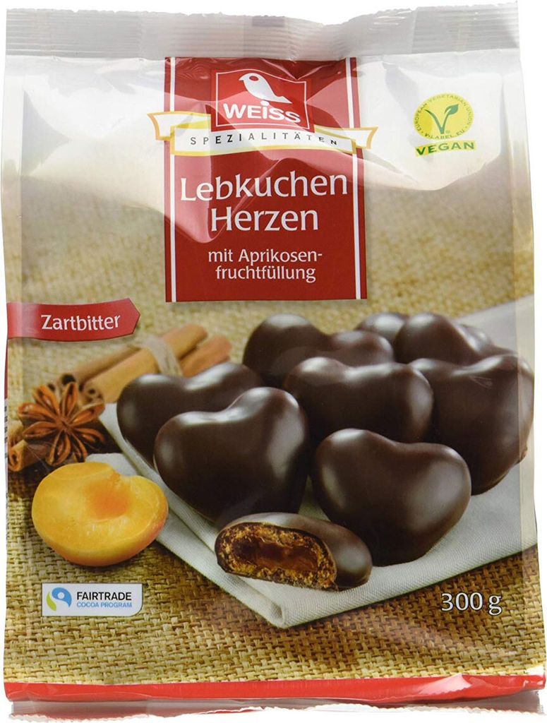 A package of heart-shaped chocolate-covered lebkuchen with apricot filling, along with some ingredients like star anise, cinnamon sticks, and an apricot half.