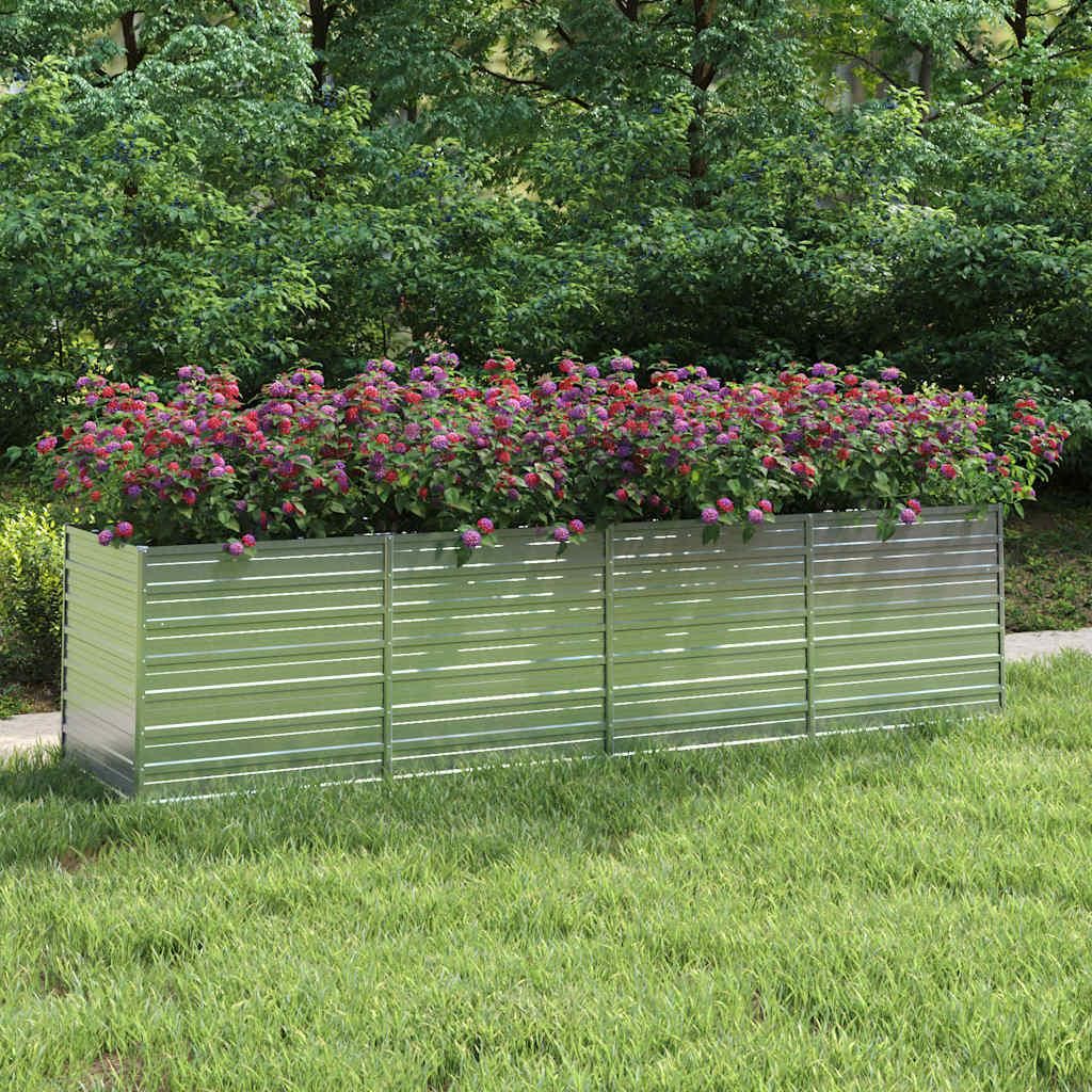A raised garden bed filled with flowering plants sits on a lawn, with trees in the background.