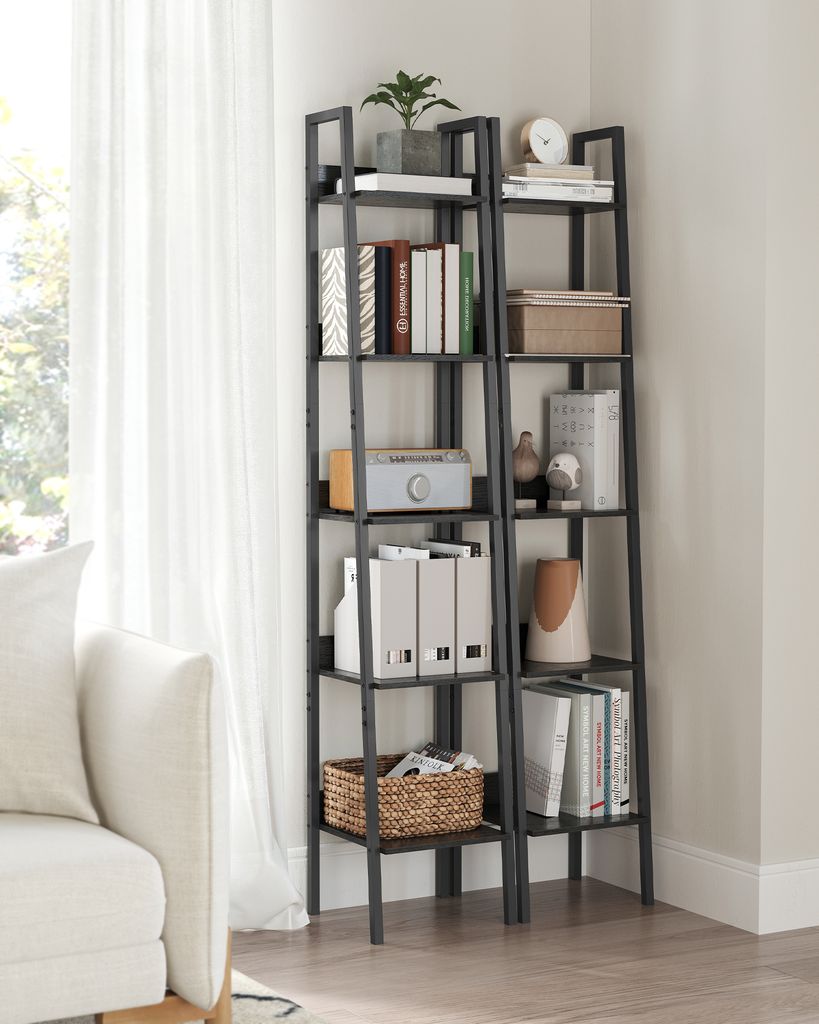 A tall, narrow ladder bookshelf filled with books and decorative items, placed next to a white sofa and in front of a window with sheer curtains.