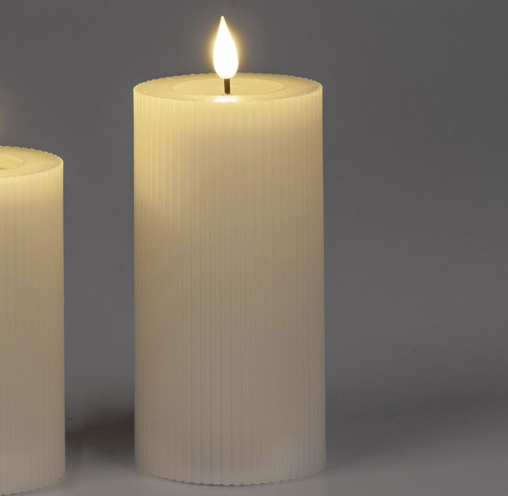 Two cream-colored LED candles with ribbed texture are shown against a plain gray background. The candle in the foreground has a lit LED flame.