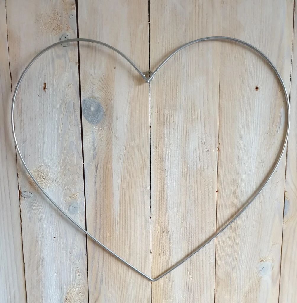 A silver metal heart-shaped wire frame is centered on a light-colored wooden plank background.