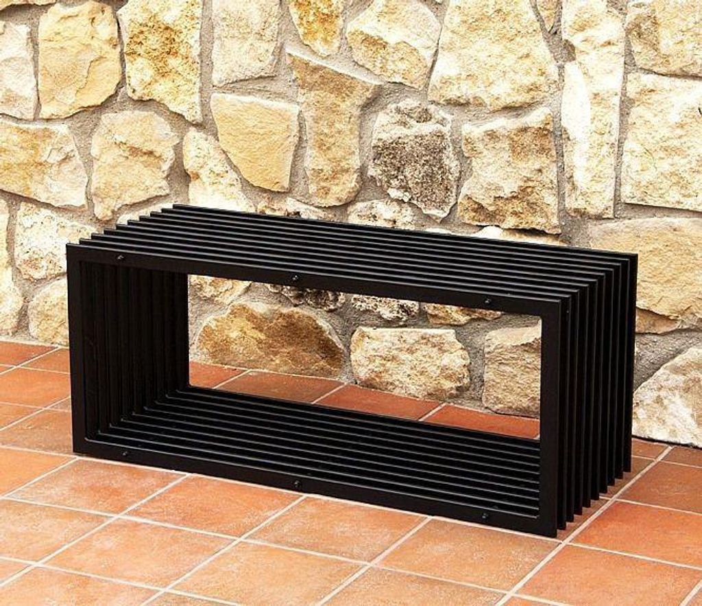 A black metal bench is placed on a tiled patio in front of a stone wall.