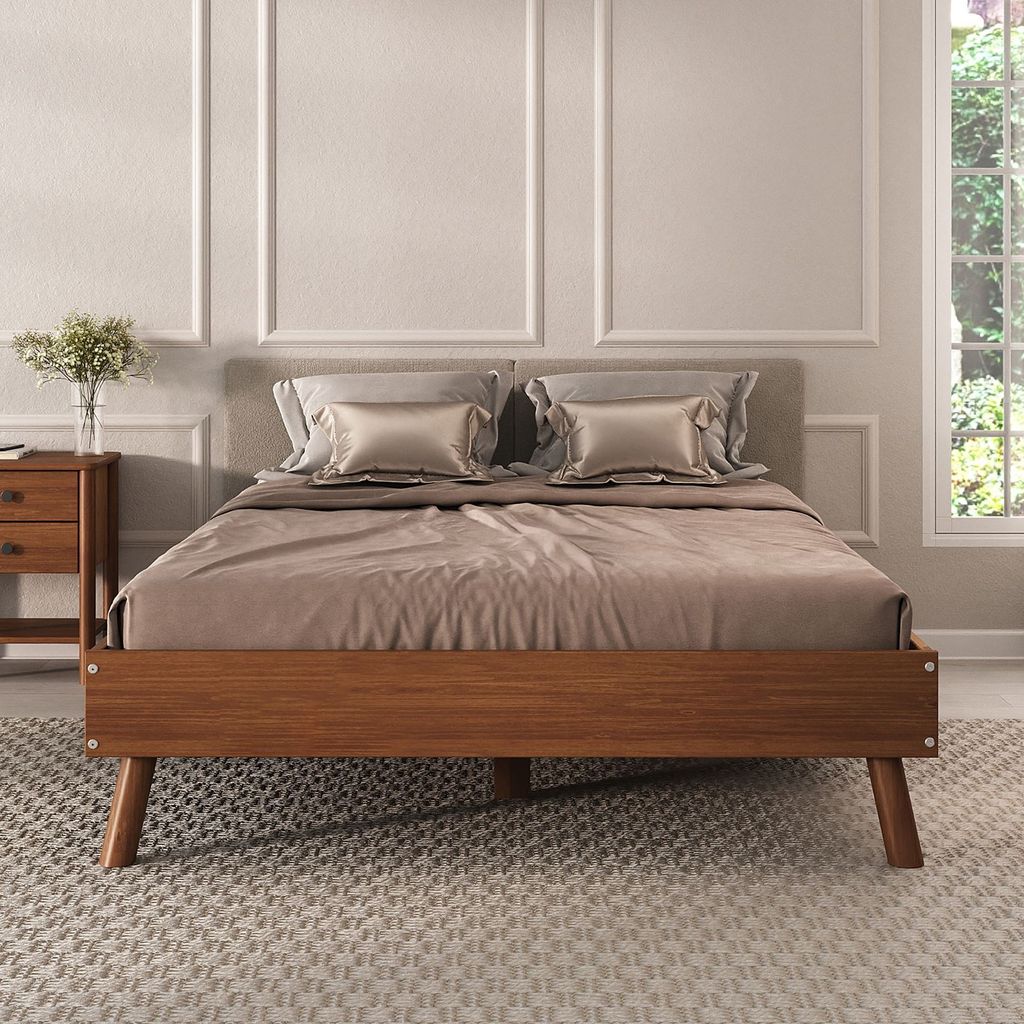 A bed with wooden frame and brown bedding is shown in a room with decorative wall panels and a window with greenery outside.