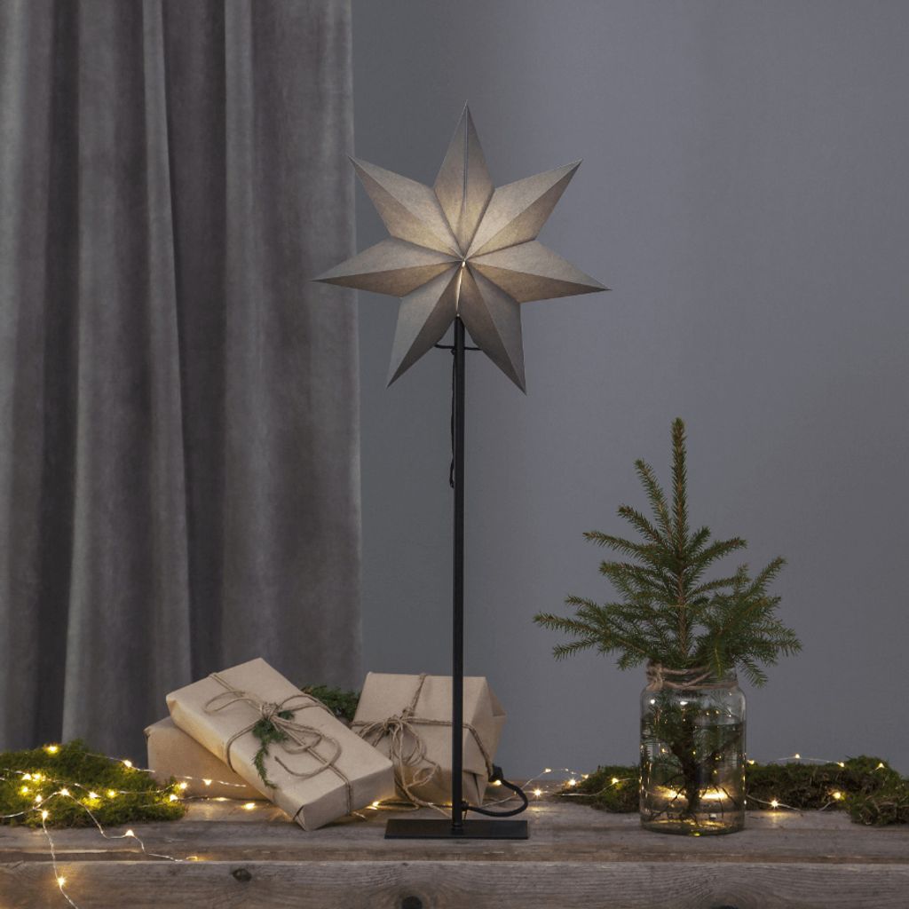 A star-shaped lamp is displayed on a wooden surface with gifts and a small Christmas tree, suggesting a festive or decorative setting.
