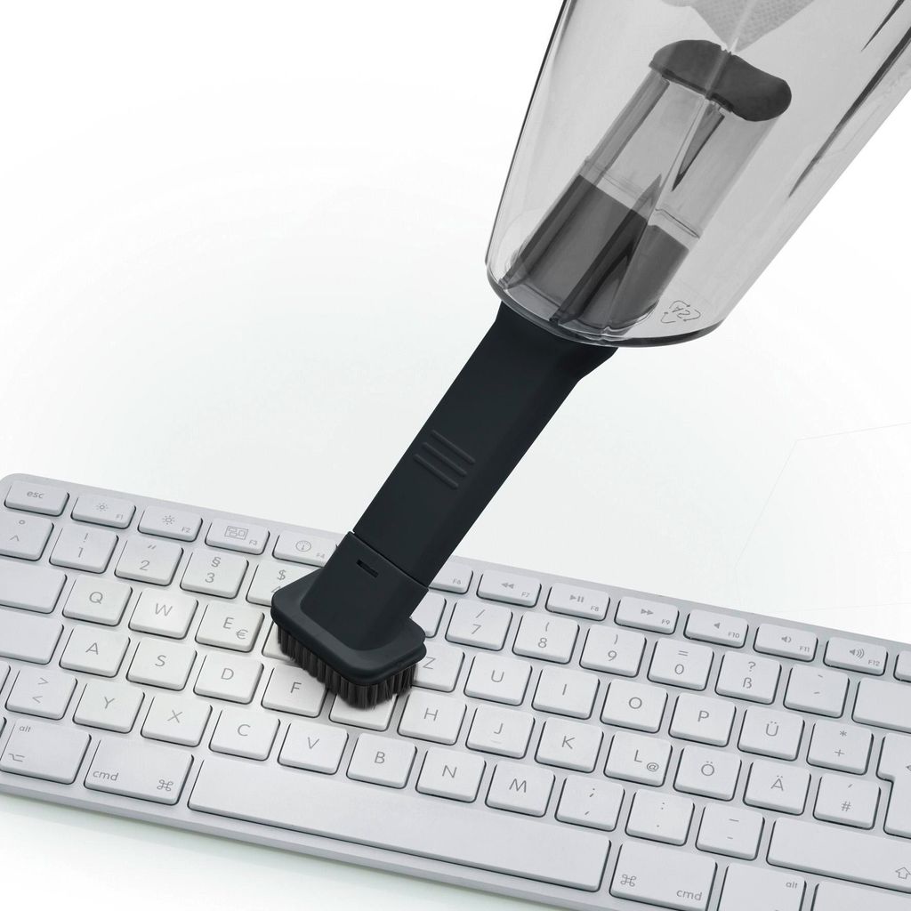 A mini vacuum cleaner with a brush attachment is being used to clean a computer keyboard.