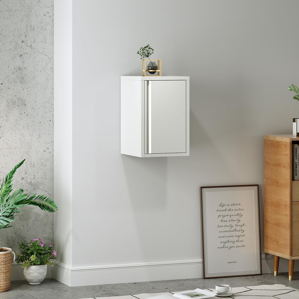 A white wall-mounted cabinet with a mirrored door is shown in a room setting, with plants and a framed picture visible.