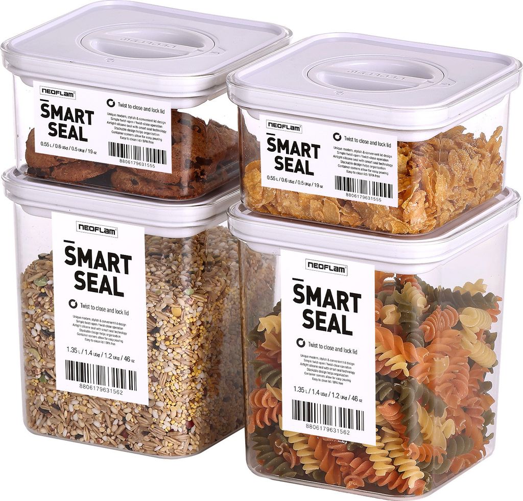Four clear plastic food storage containers with white lids, stacked in a 2x2 arrangement. Each container is filled with different food items: cookies, cereal, grains, and pasta. Labels are visible on the front of each container.