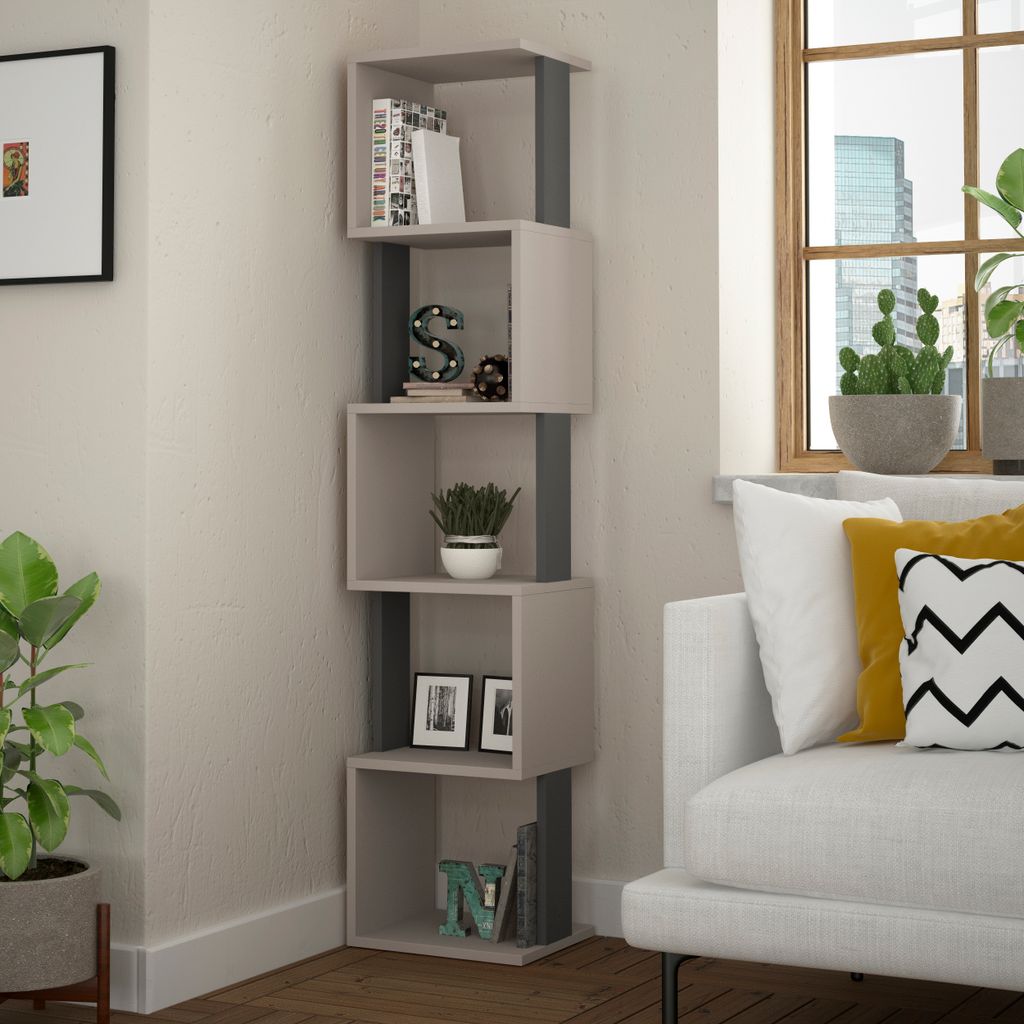 A corner bookshelf filled with books and decorative items, next to a window with plants and a sofa.