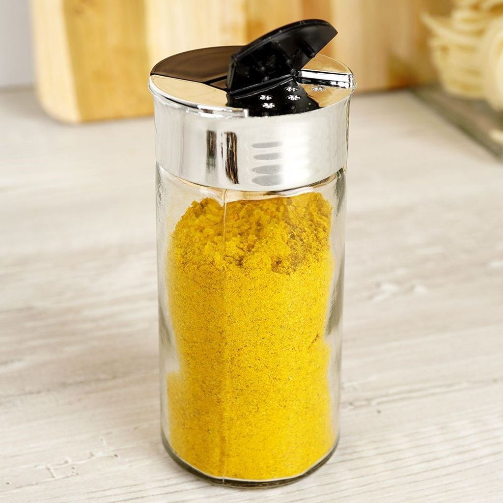 A close-up shot of a spice jar filled with yellow powder, placed on a light-colored wooden surface.