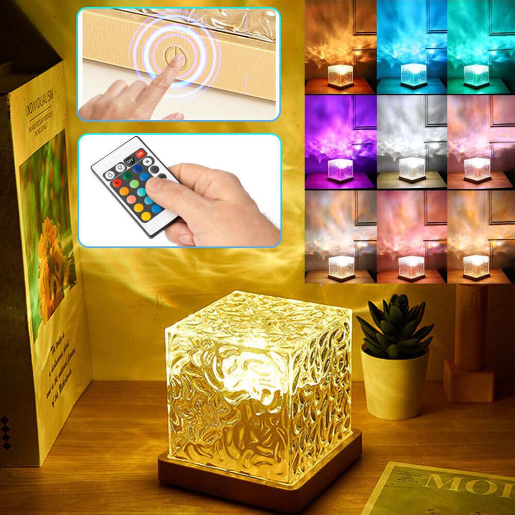 A collage of images showing a cube-shaped lamp with a textured surface, a remote control, and various color light projections. The main image shows the lamp on a wooden surface with a plant and a book.