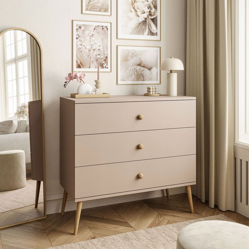 A dresser with three drawers is placed in a room with artwork on the wall and a large mirror.