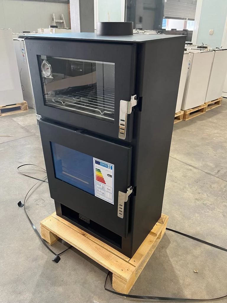 A black wood-burning stove is shown in a warehouse or workshop setting, resting on a wooden pallet.