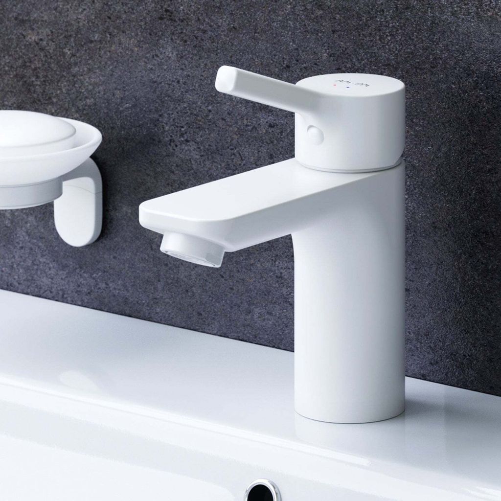 A white bathroom faucet and soap dish are shown against a dark gray tiled wall and a white countertop.