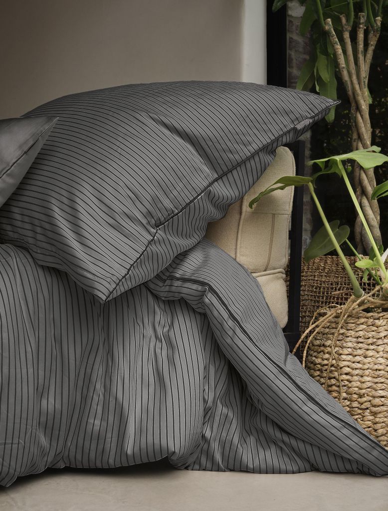 A close-up view of a grey striped duvet and pillowcase set, with a woven basket and plant in the background.