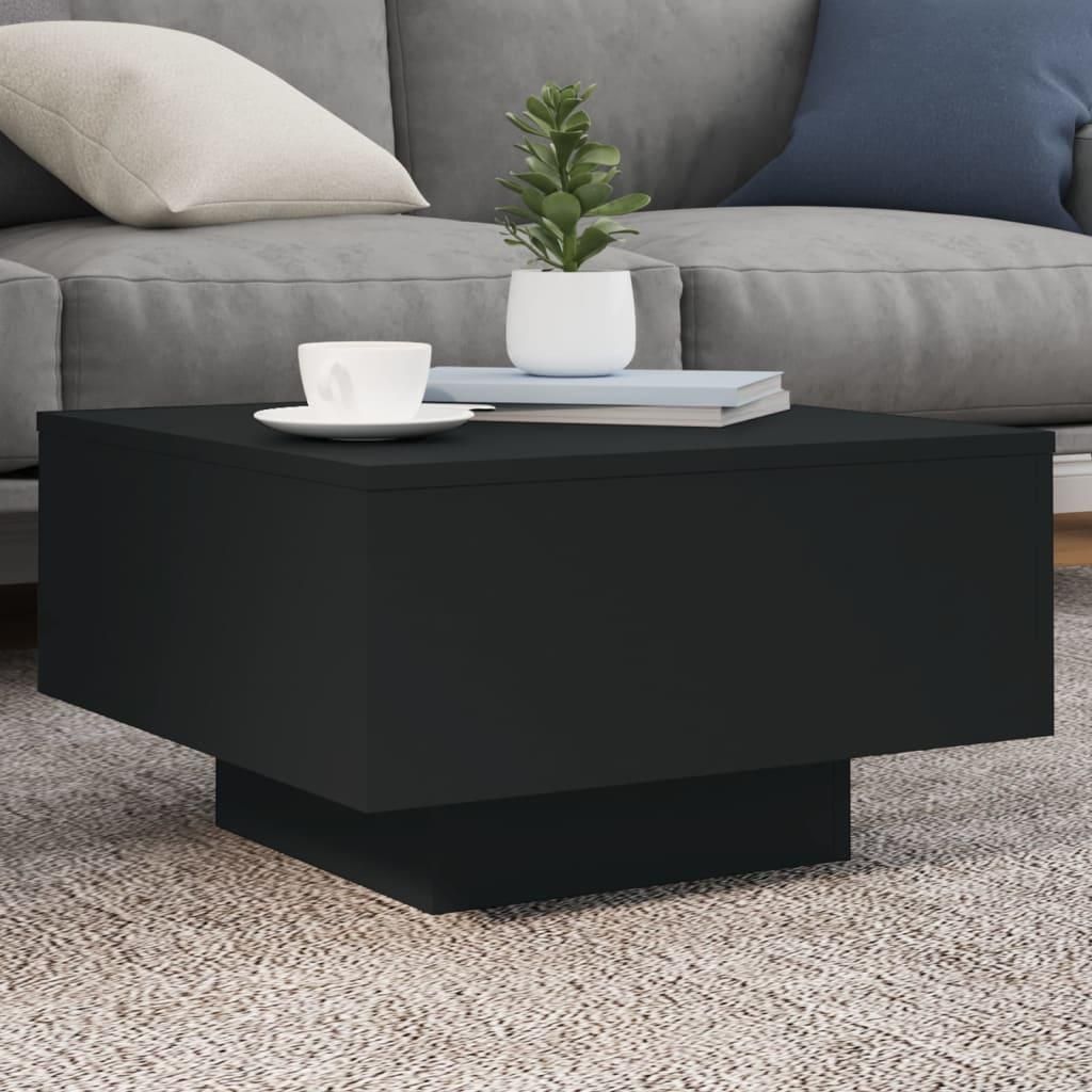 A black coffee table with a cup and a plant on it, placed on a rug in front of a sofa.