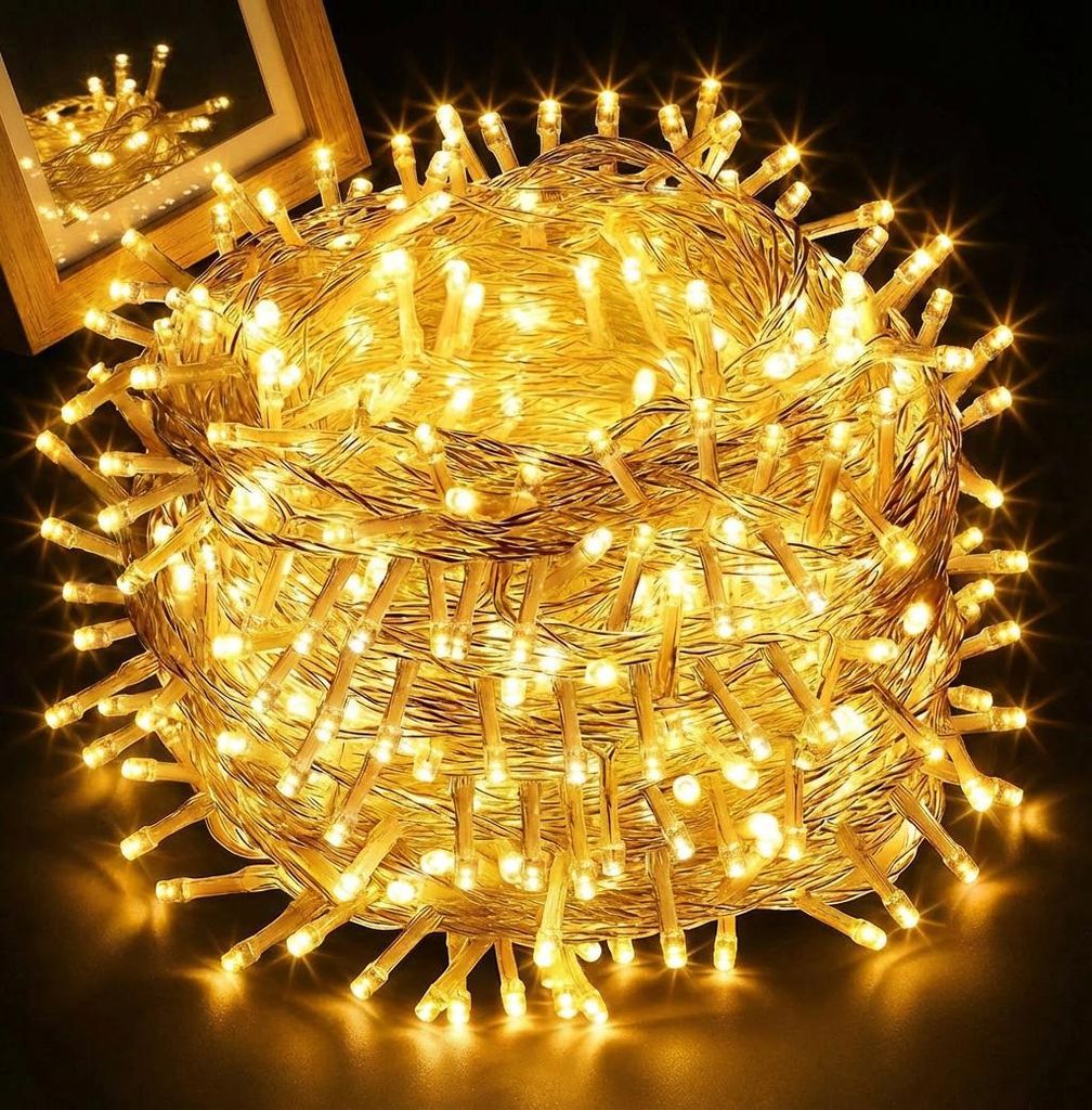 A tightly wound ball of yellow LED string lights, with a wooden frame and reflection visible in the background.