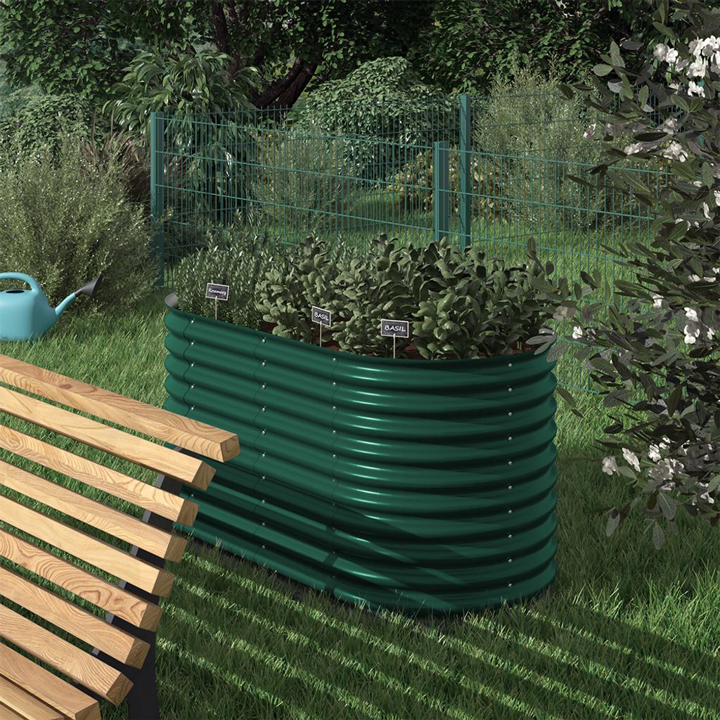A green raised garden bed filled with herbs sits in a garden next to a wooden bench.