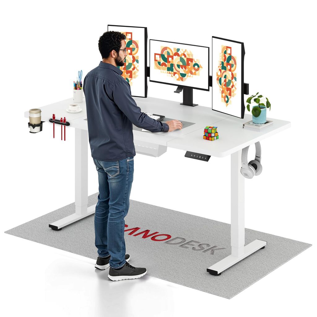 A man stands at a white standing desk with multiple monitors, accessories, and a rug underneath.
