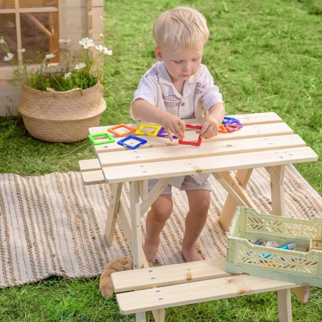 A young child playing with magnetic shapes on a wooden picnic table outdoors.