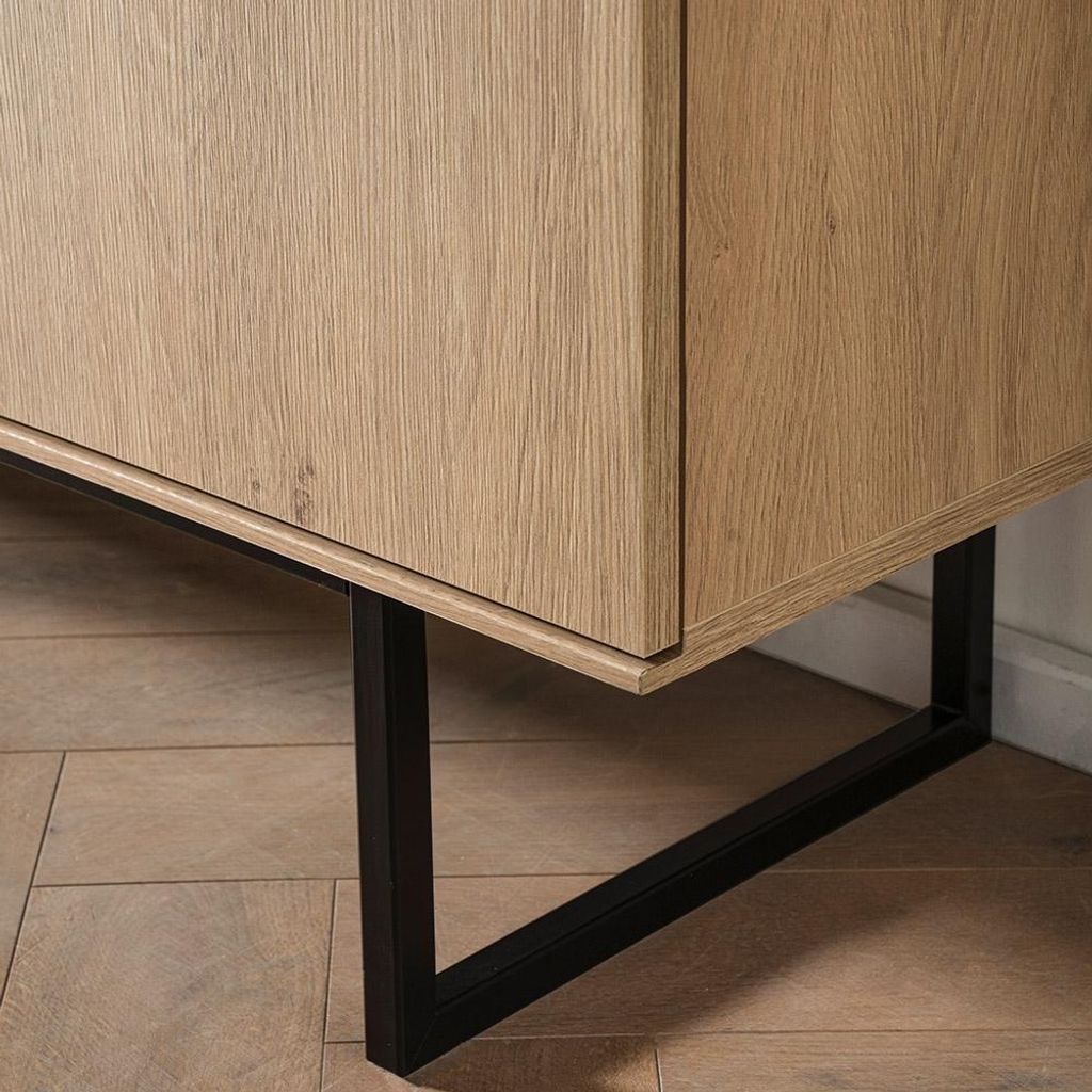 A close-up shot of the bottom corner of a wooden sideboard with a black metal leg.