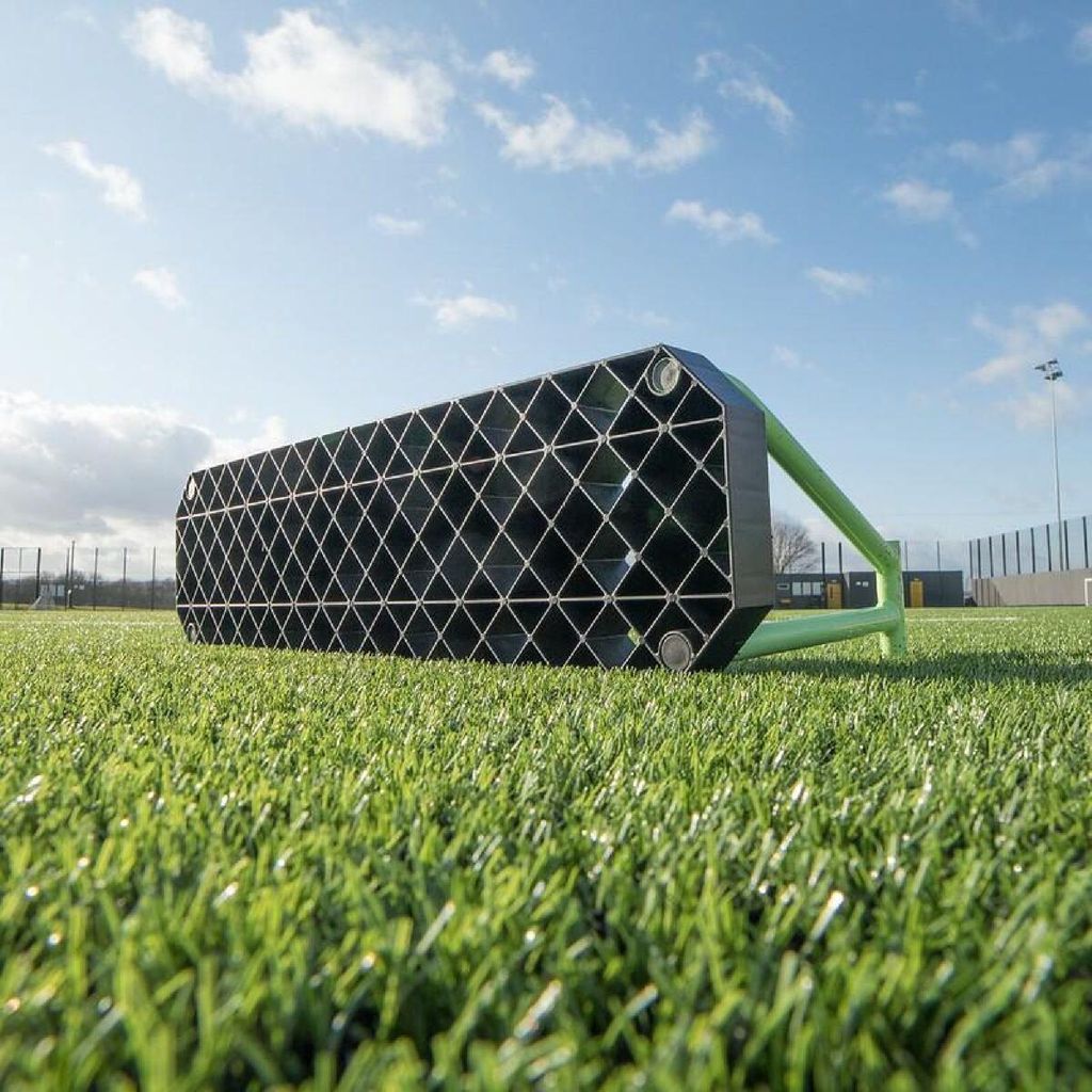 A black and green soccer goal is lying on its side on artificial turf.