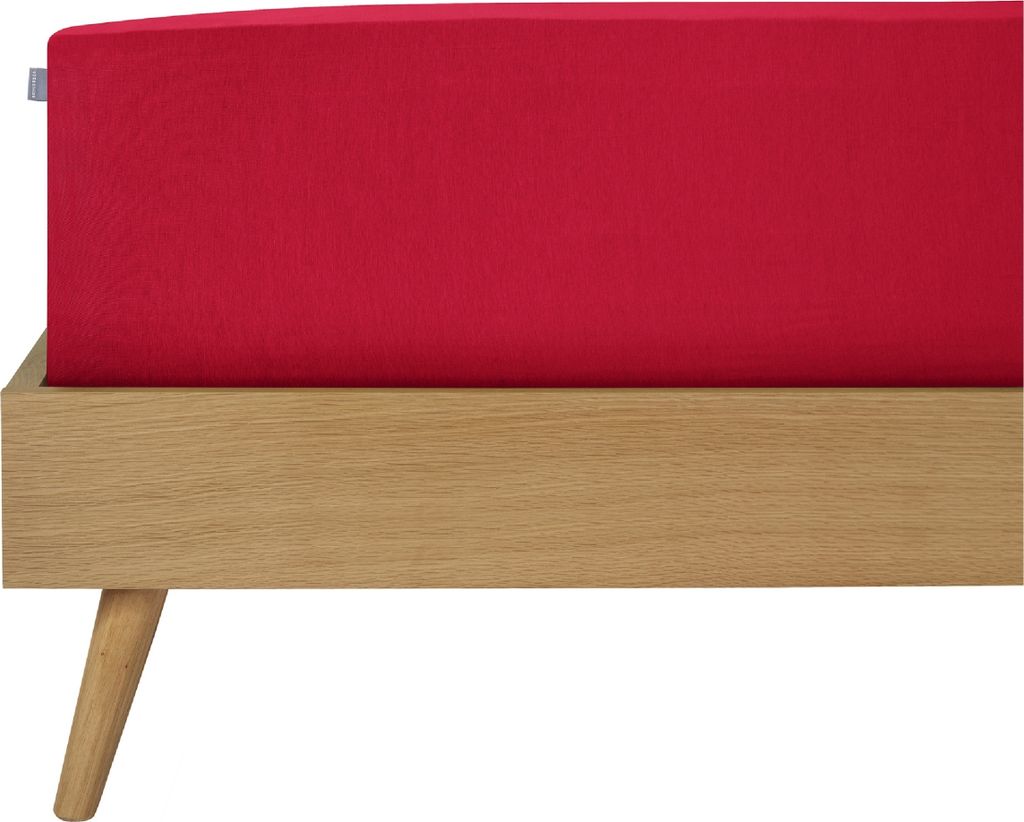 A close-up view of a red fitted sheet on a wooden bed frame.