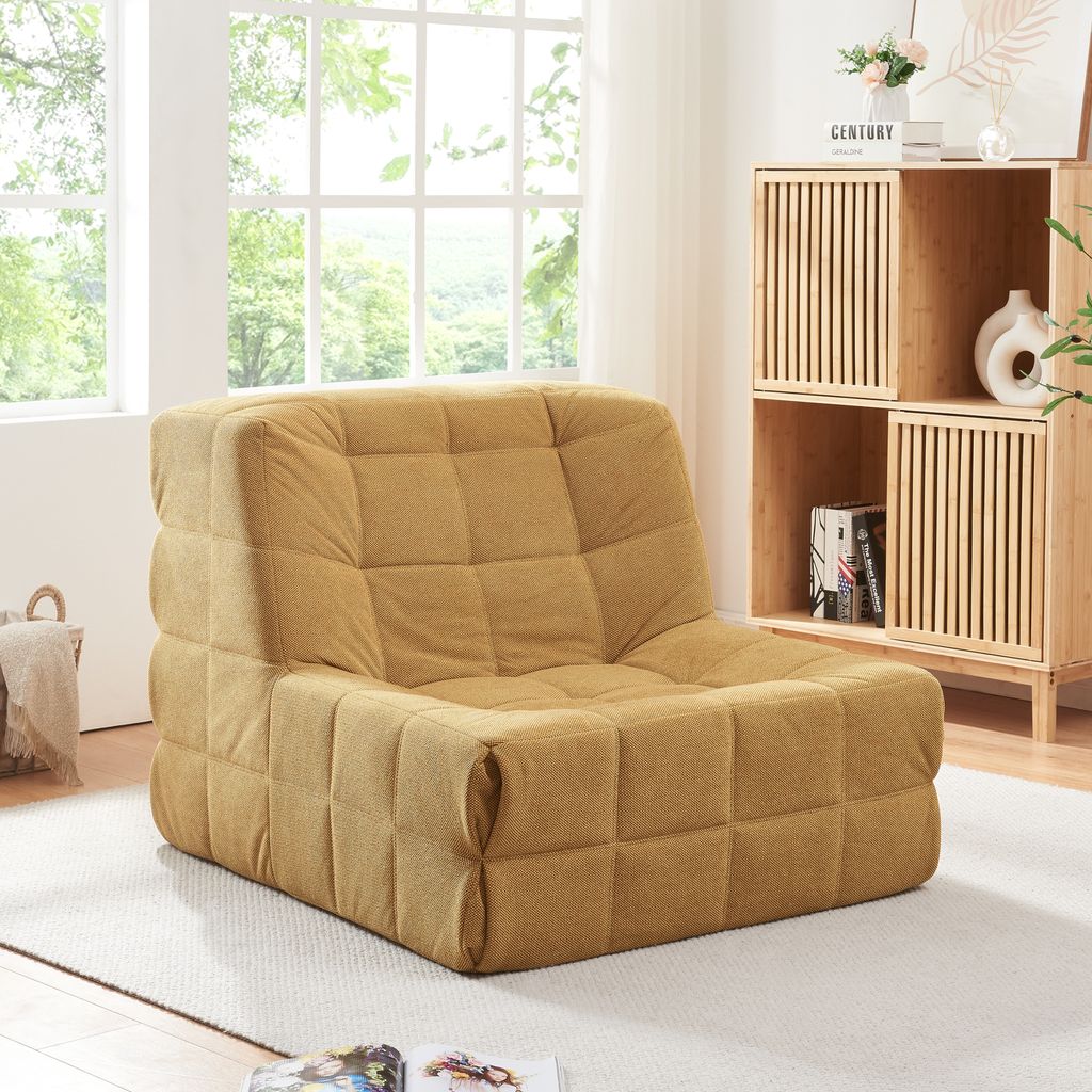 A yellow upholstered floor chair is placed on a rug in a well-lit room with a large window and a wooden shelving unit.