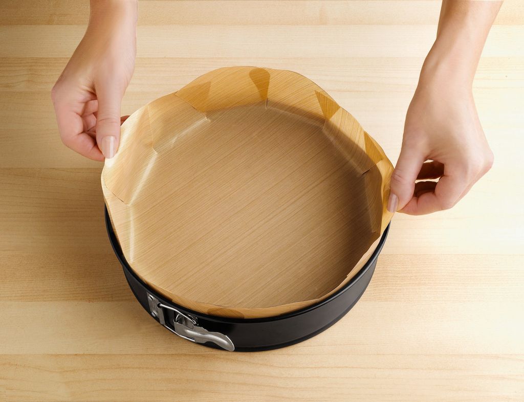 Hands lining a springform pan with parchment paper.