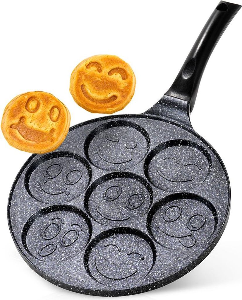 A frying pan with seven smiley face molds, with two smiley face pancakes next to it.