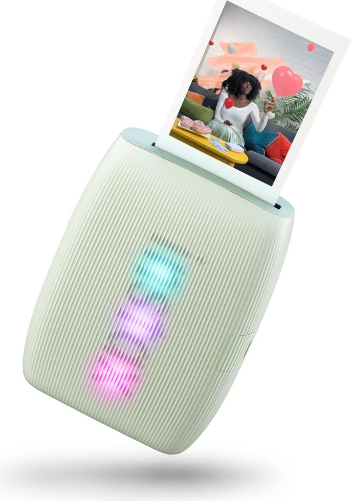 A mint green Instax mini Link 3 photo printer is shown at an angle, printing a photo of a woman holding a heart-shaped balloon. The printer has three illuminated lights in blue, pink, and purple.