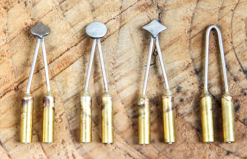 A set of five different metal tips for a wood-burning tool, laid out on a wooden surface.