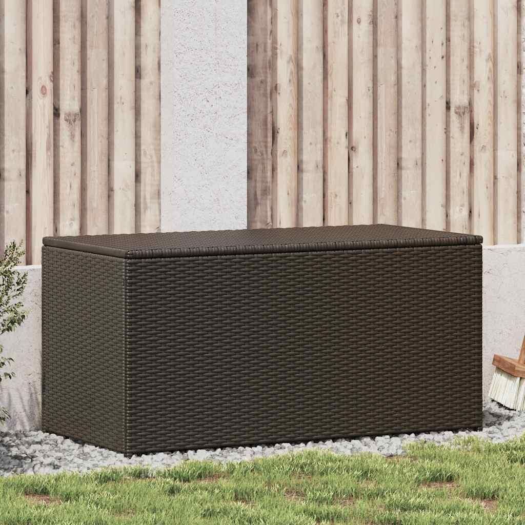 A brown poly rattan garden box is placed on gravel and grass in front of a wooden fence and a textured wall.